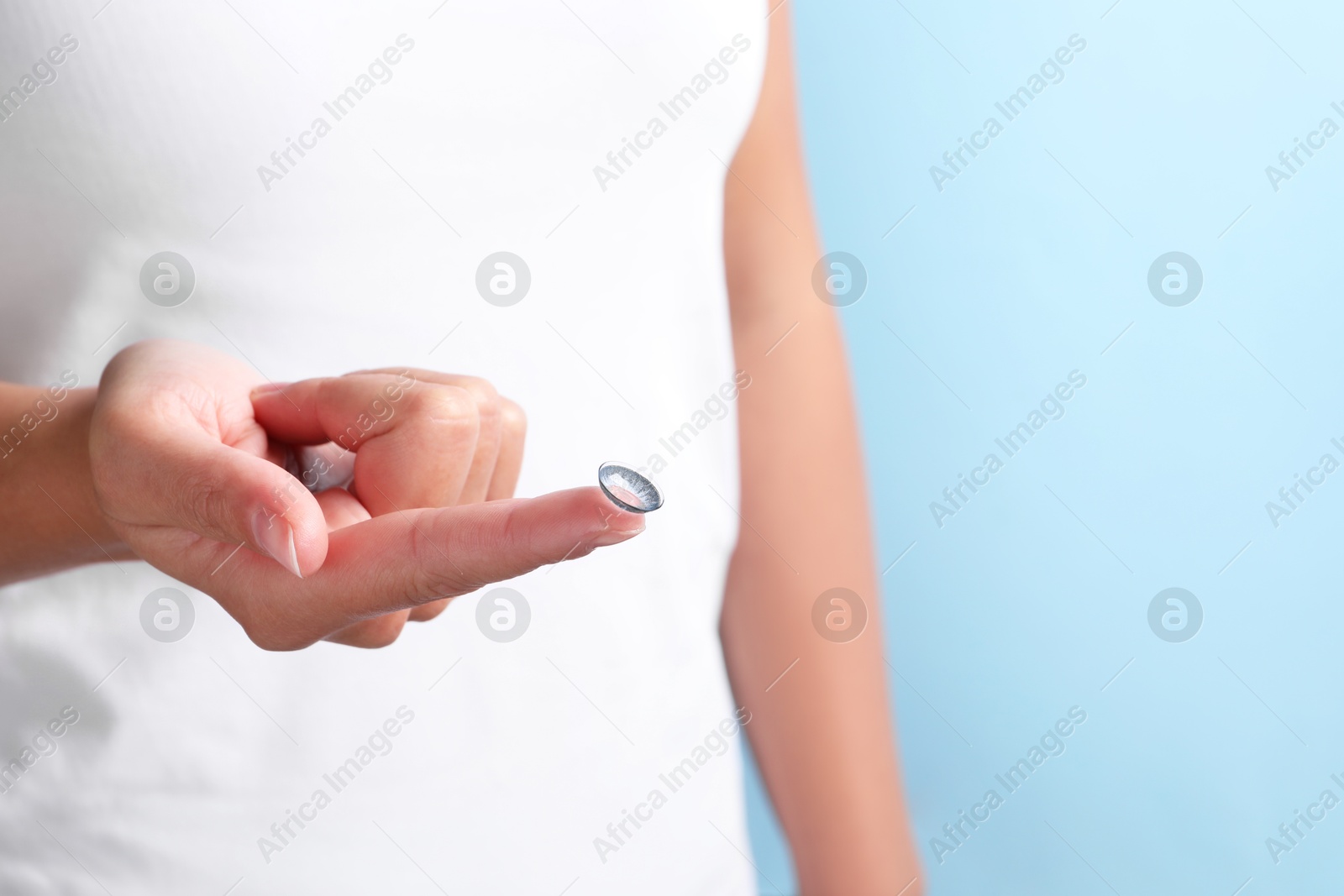 Photo of Woman holding color contact lens on light blue background, closeup