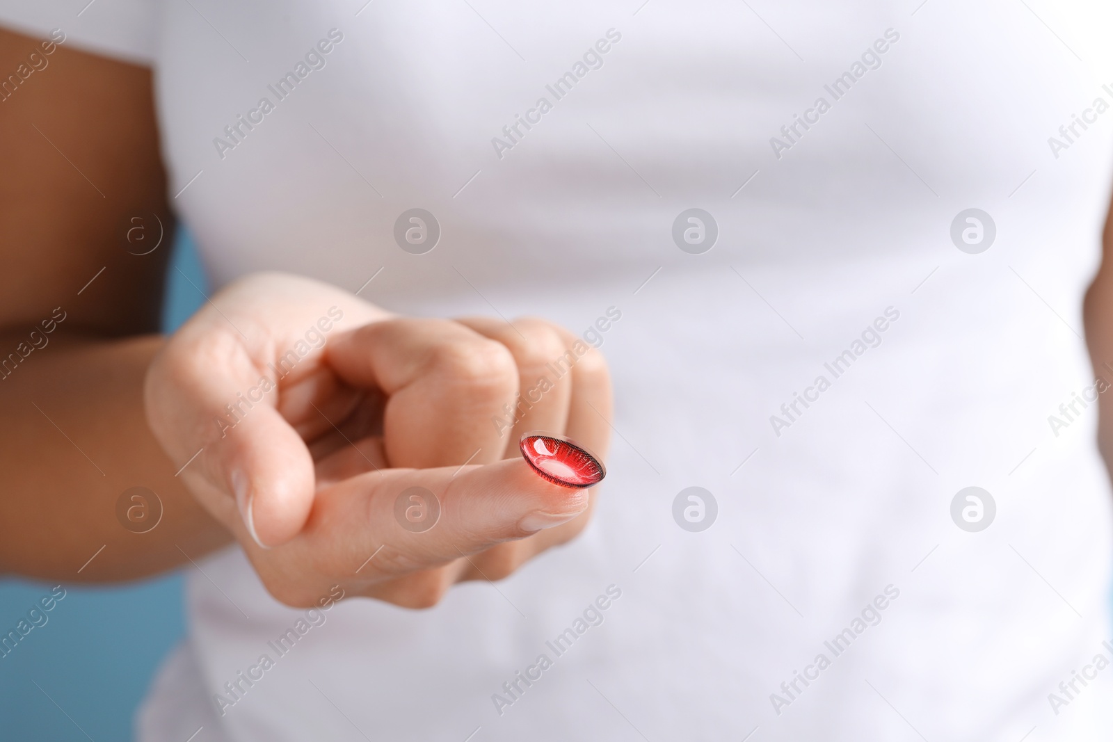 Photo of Woman holding color contact lens on light blue background, closeup