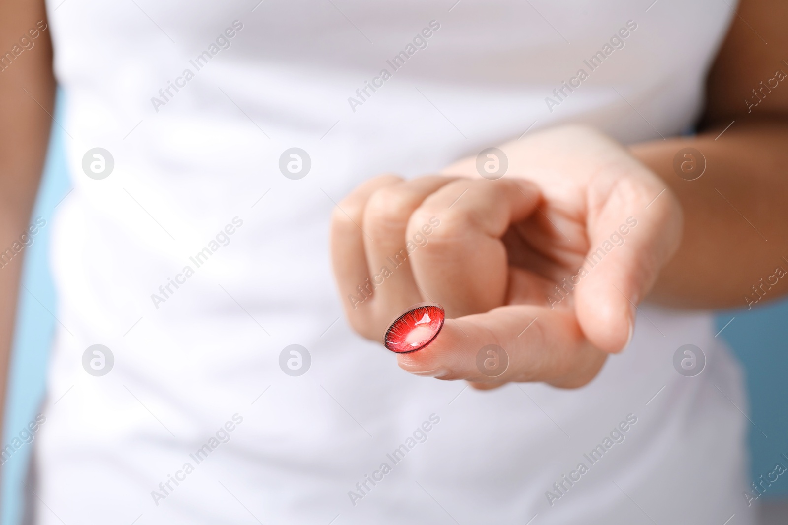 Photo of Woman holding color contact lens on light blue background, closeup