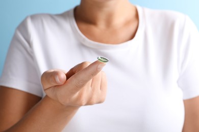 Photo of Woman holding color contact lens on light blue background, closeup