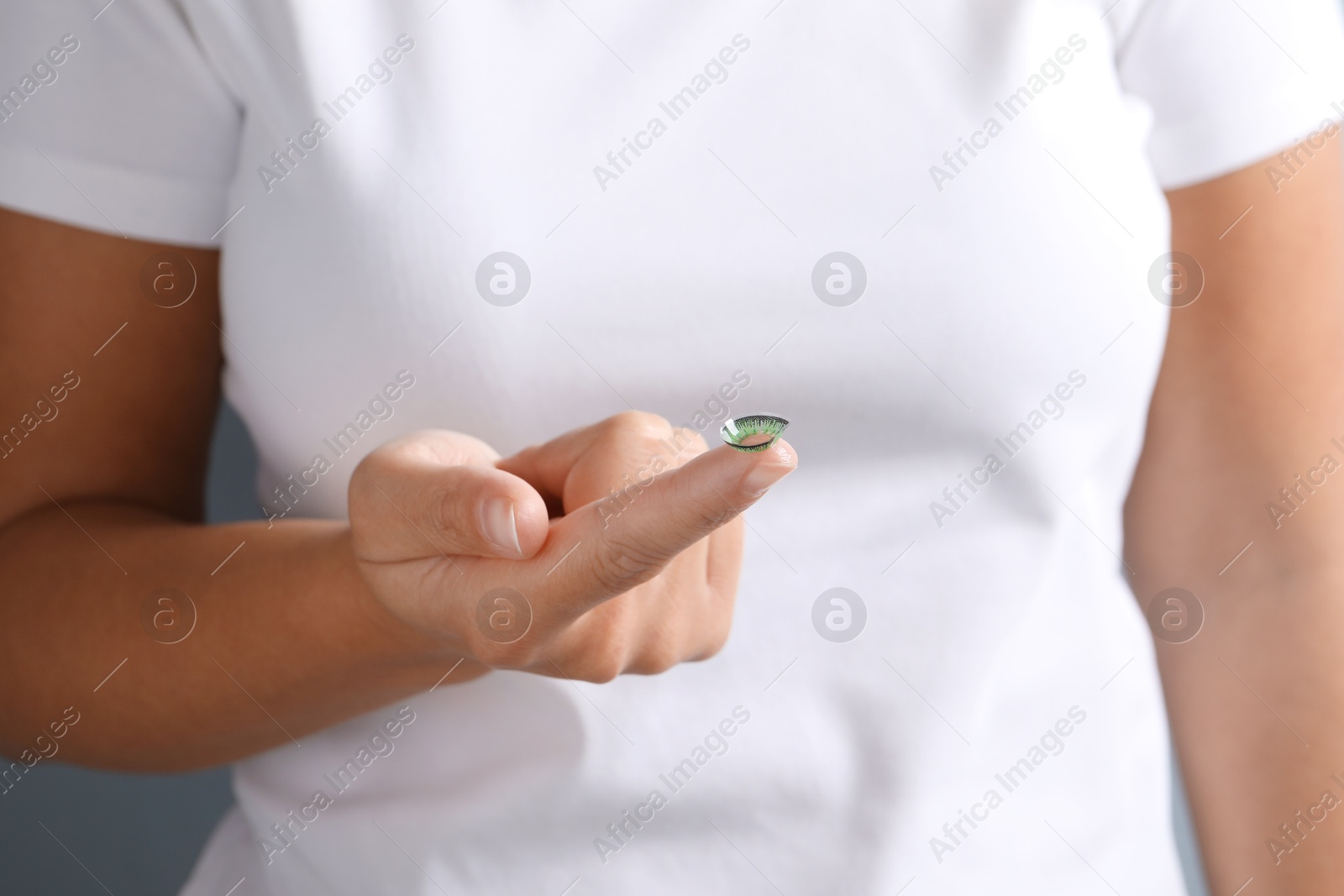 Photo of Woman holding color contact lens on light background, closeup