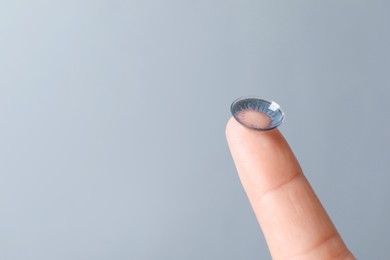 Photo of Woman holding color contact lens on light grey background, closeup. Space for text