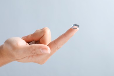 Photo of Woman holding color contact lens on light grey background, closeup