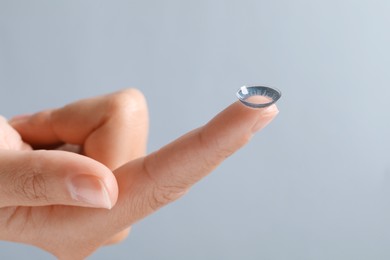 Photo of Woman holding color contact lens on light grey background, closeup