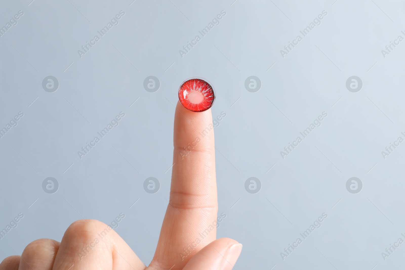 Photo of Woman holding color contact lens on light grey background, closeup