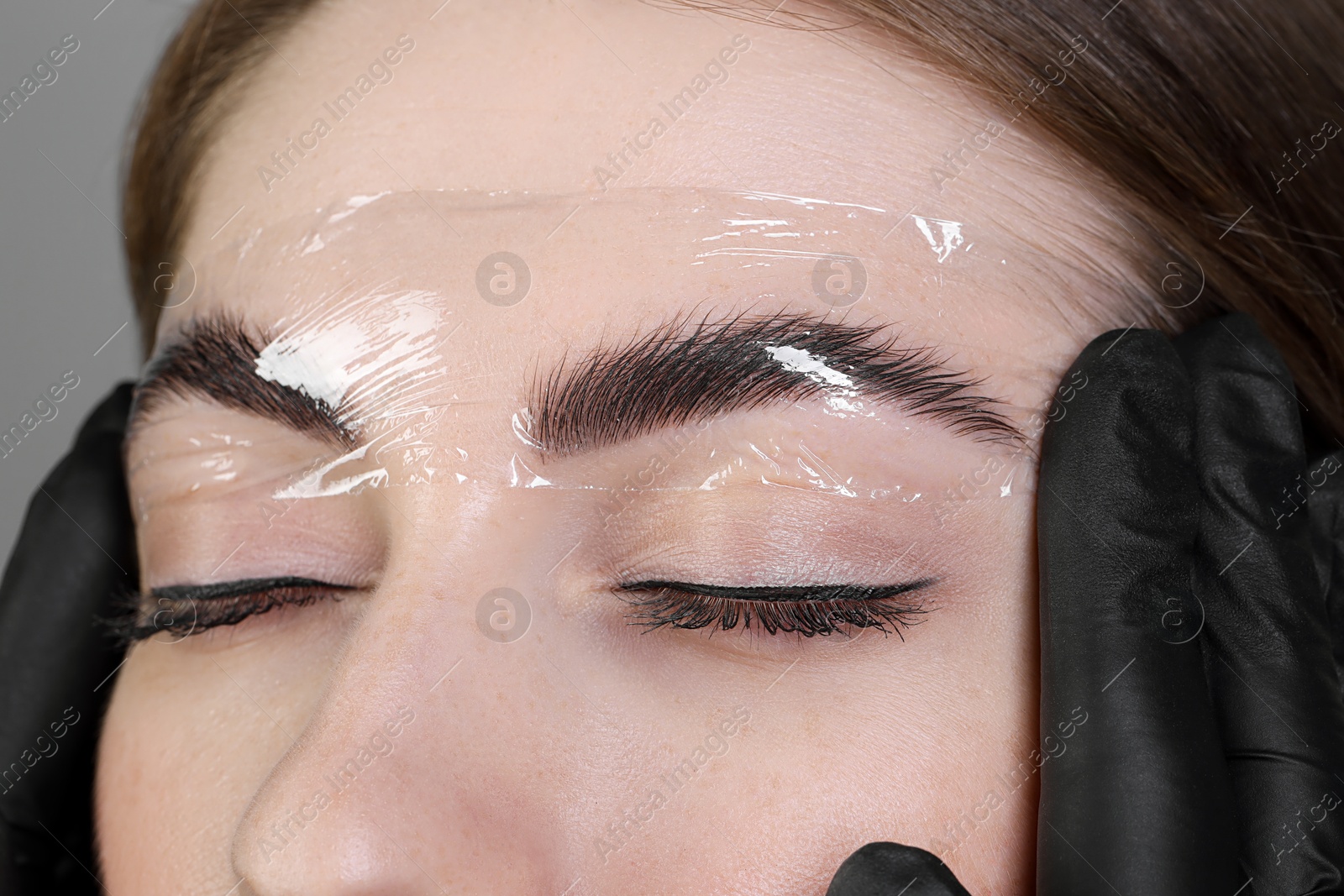 Photo of Brow lamination. Cosmetologist putting film onto woman's eyebrows, closeup