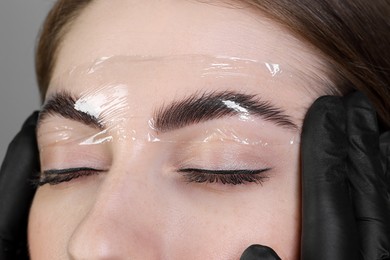 Photo of Brow lamination. Cosmetologist putting film onto woman's eyebrows, closeup