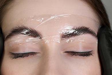 Photo of Brow lamination. Cosmetologist putting film onto woman's eyebrows, closeup