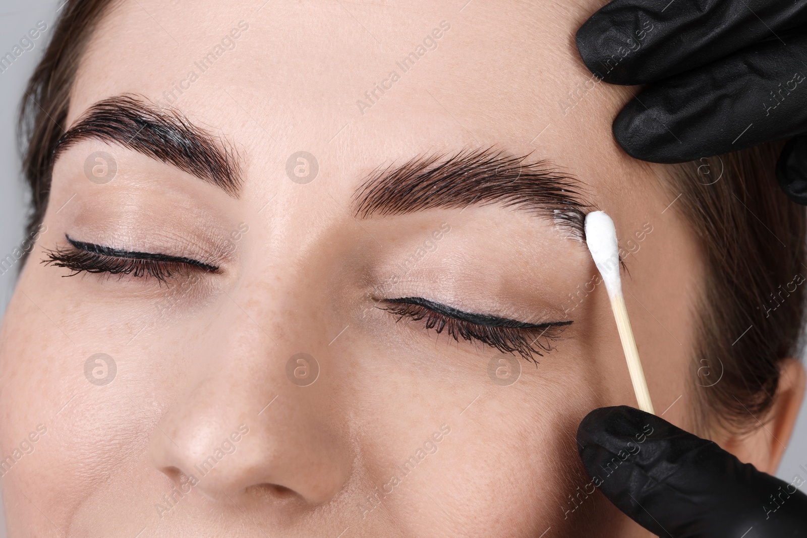 Photo of Brow lamination. Cosmetologist applying cream onto woman's eyebrows, closeup