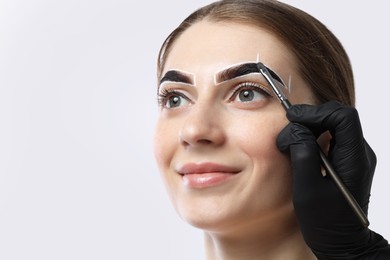 Photo of Young woman undergoing henna eyebrows dyeing on light background, closeup. Space for text