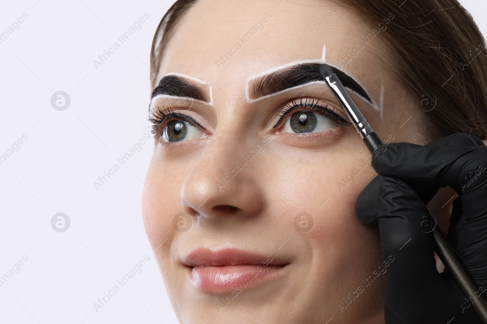 Photo of Young woman undergoing henna eyebrows dyeing on light background, closeup