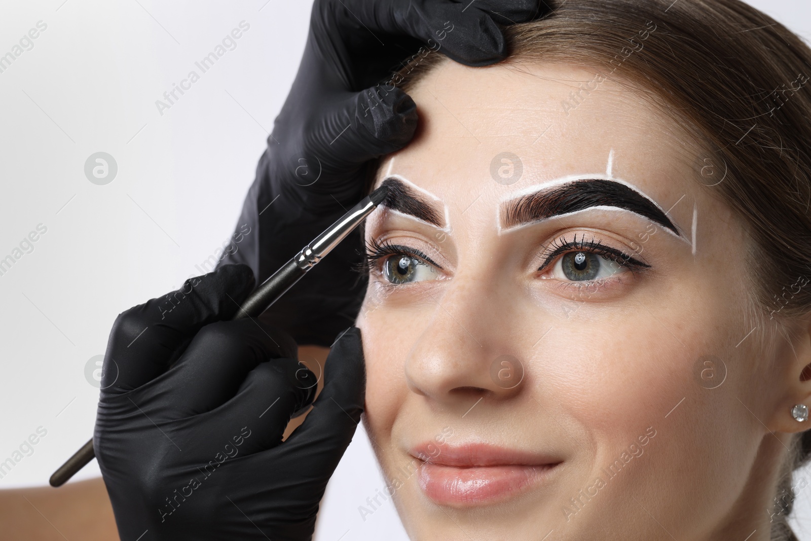 Photo of Young woman undergoing henna eyebrows dyeing on light background, closeup