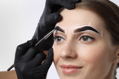 Photo of Young woman undergoing henna eyebrows dyeing on light background, closeup