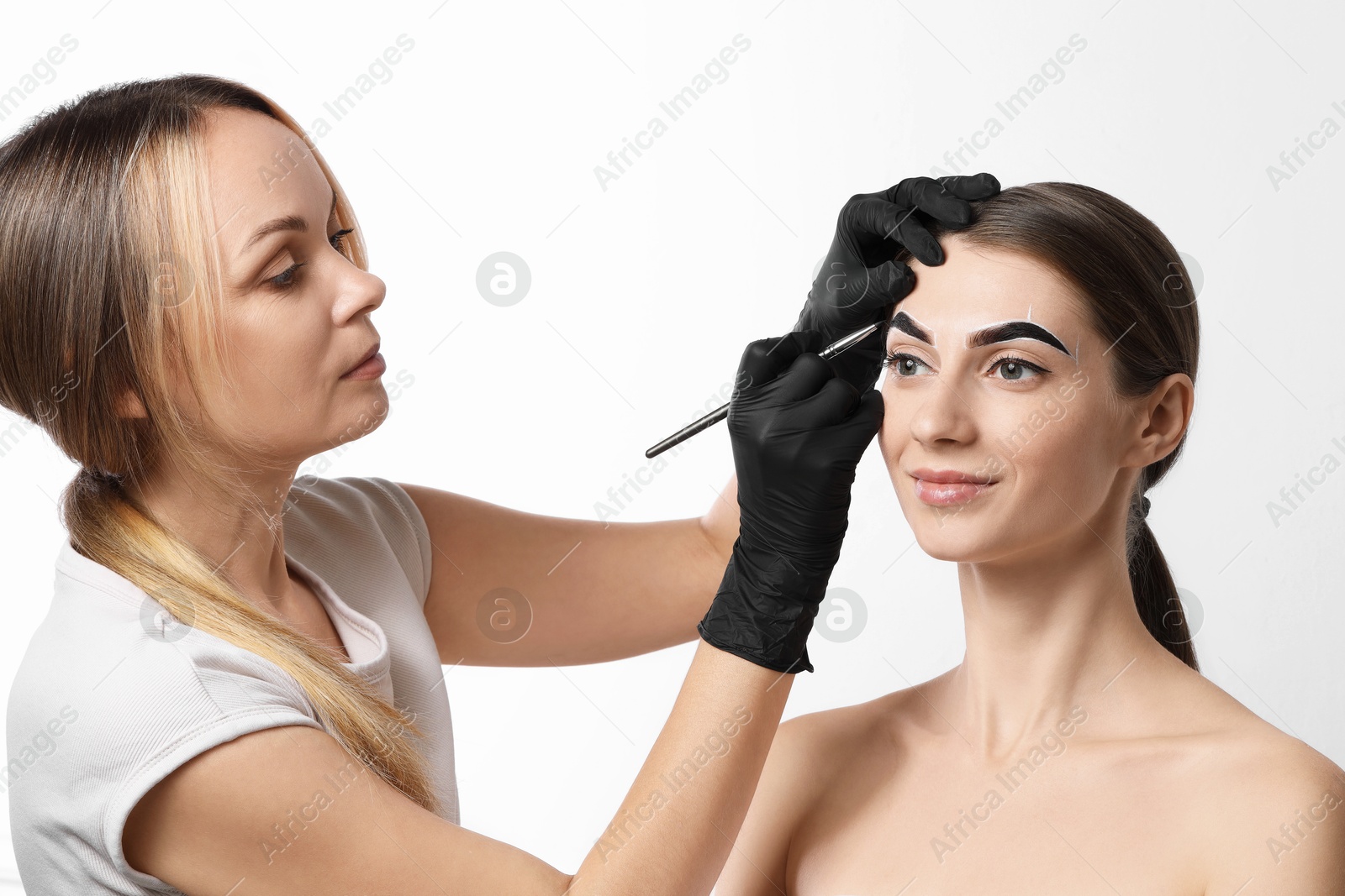 Photo of Beautician dyeing client’s eyebrows with henna on light background