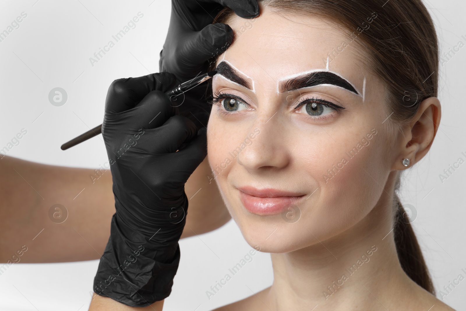 Photo of Young woman undergoing henna eyebrows dyeing procedure on light background, closeup