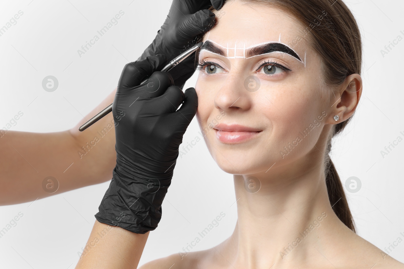 Photo of Young woman undergoing henna eyebrows dyeing procedure on white background, closeup