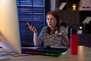 Emotional girl playing video game with keyboard and mouse at table indoors