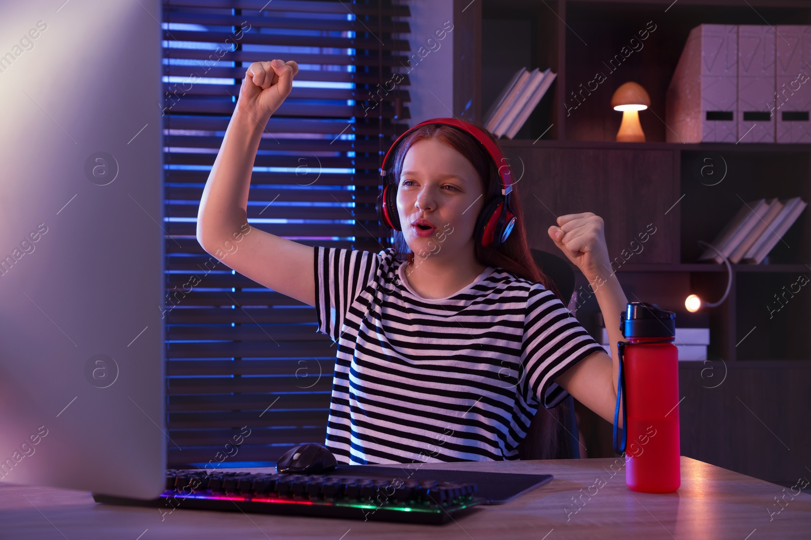 Photo of Emotional girl playing video game with keyboard and mouse at table indoors