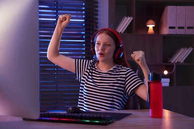 Photo of Emotional girl playing video game with keyboard and mouse at table indoors