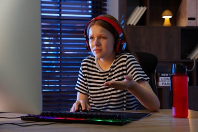 Emotional girl playing video game with keyboard and mouse at table indoors