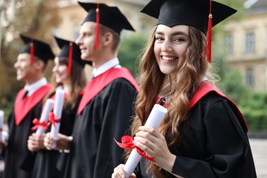 Photo of Happy students with diplomas after graduation ceremony outdoors, selective focus