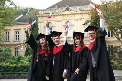 Happy students with diplomas after graduation ceremony outdoors