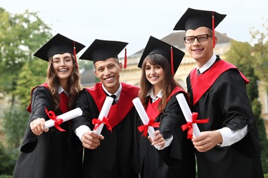 Happy students with diplomas after graduation ceremony outdoors