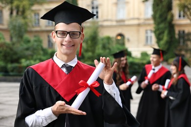 Photo of Happy students with diplomas after graduation ceremony outdoors, selective focus