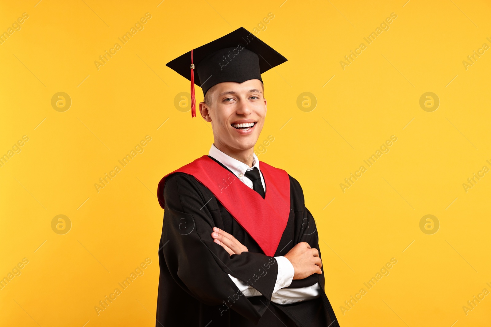 Photo of Happy student with crossed arms after graduation on orange background