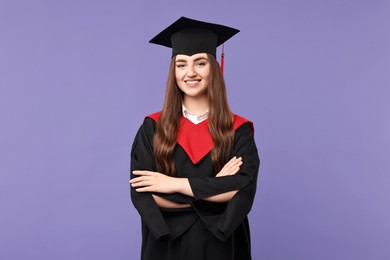 Happy student with crossed arms after graduation on violet background