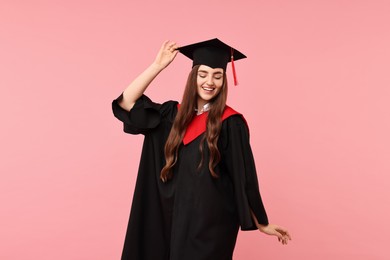 Happy student after graduation on pink background