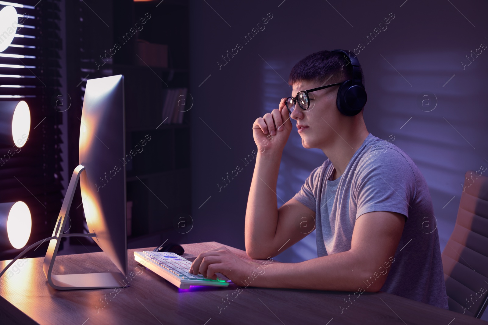 Photo of Young man playing video game with keyboard at wooden table indoors