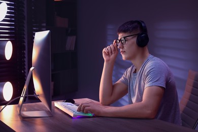 Photo of Young man playing video game with keyboard at wooden table indoors