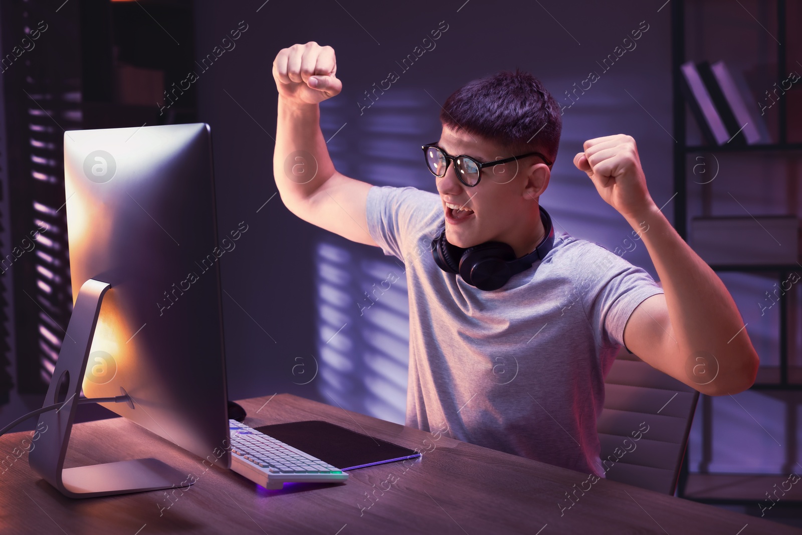 Photo of Emotional young man playing video game with keyboard at wooden table indoors