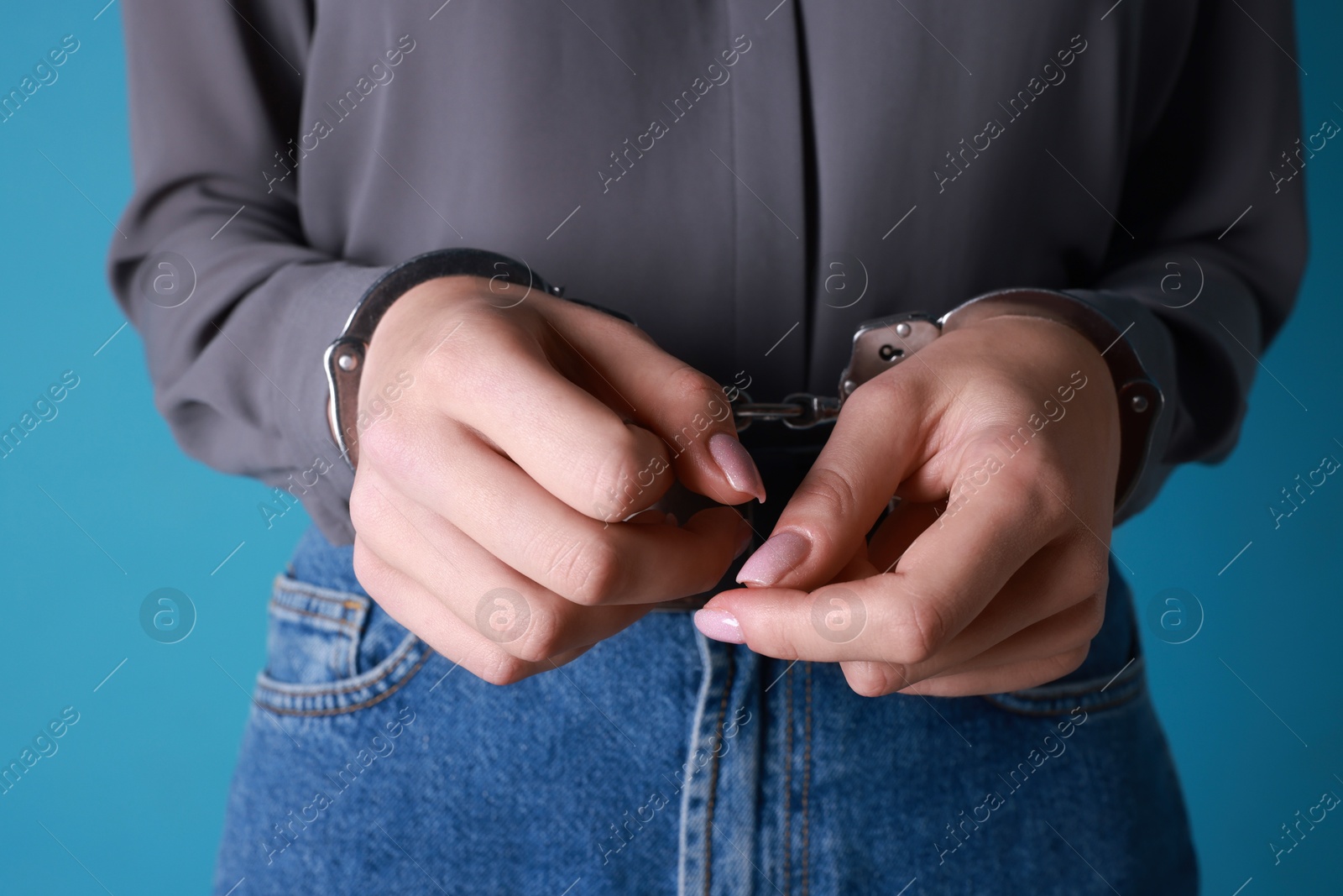 Photo of Woman in metal handcuffs on light blue background, closeup