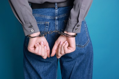 Woman in metal handcuffs on light blue background, closeup