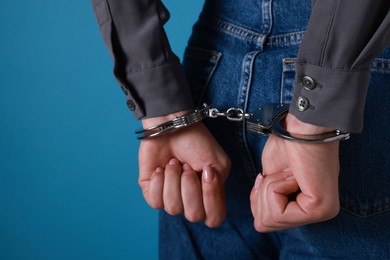 Photo of Woman in metal handcuffs on blue background, closeup. Space for text