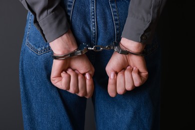 Woman in metal handcuffs on black background, closeup