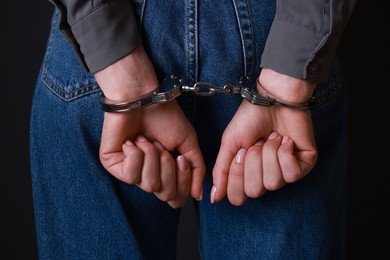 Photo of Woman in metal handcuffs on black background, closeup