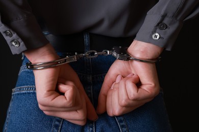 Photo of Woman in metal handcuffs on black background, closeup