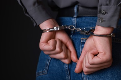 Photo of Woman in metal handcuffs on black background, closeup