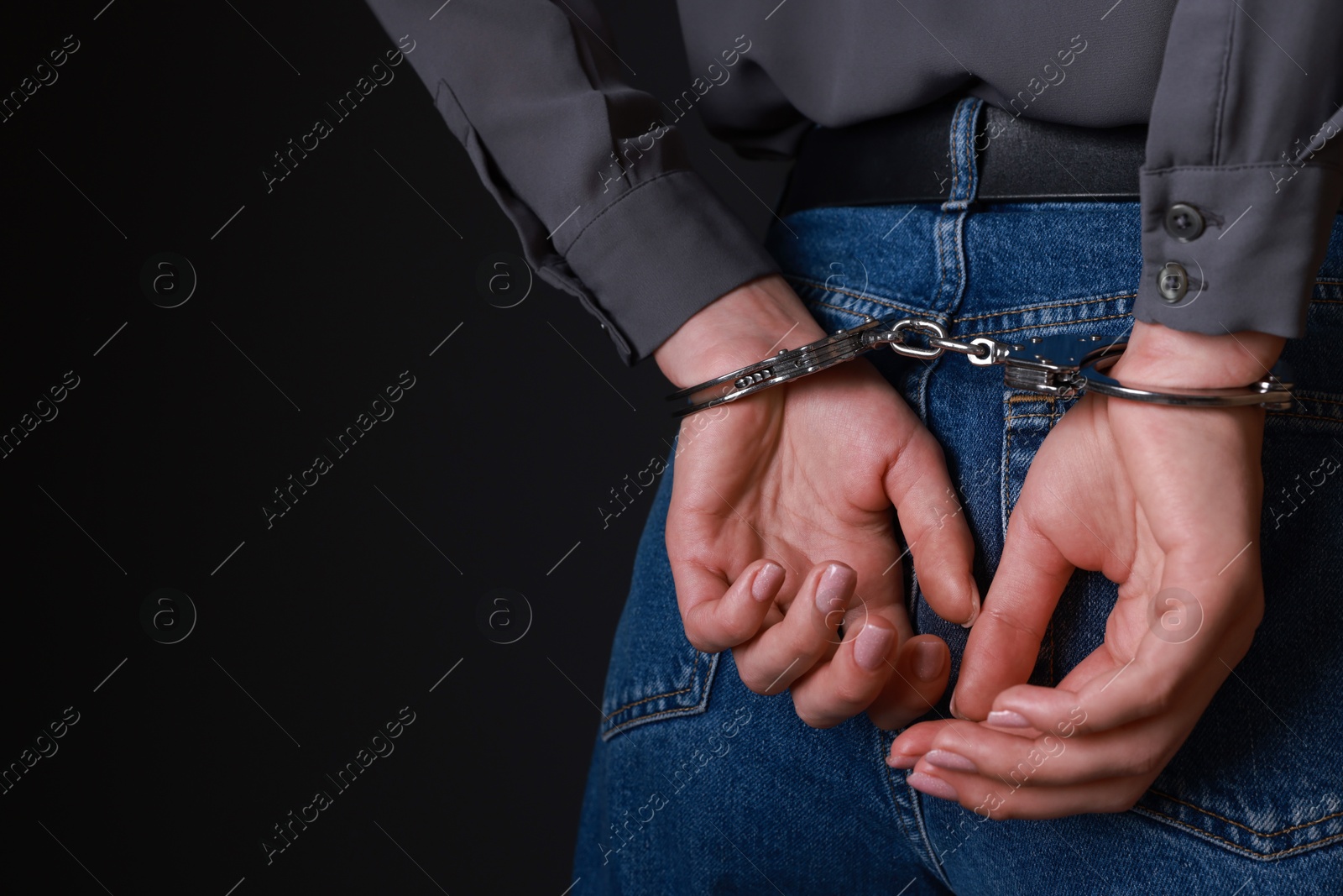 Photo of Woman in metal handcuffs on black background, closeup. Space for text