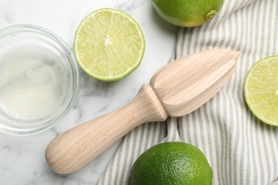 Photo of Wooden juicer and fresh limes on white marble table, flat lay