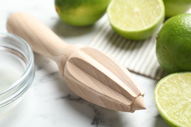 Photo of Wooden juicer and fresh limes on white marble table, closeup