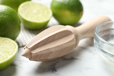 Photo of Wooden juicer and fresh limes on white marble table, closeup