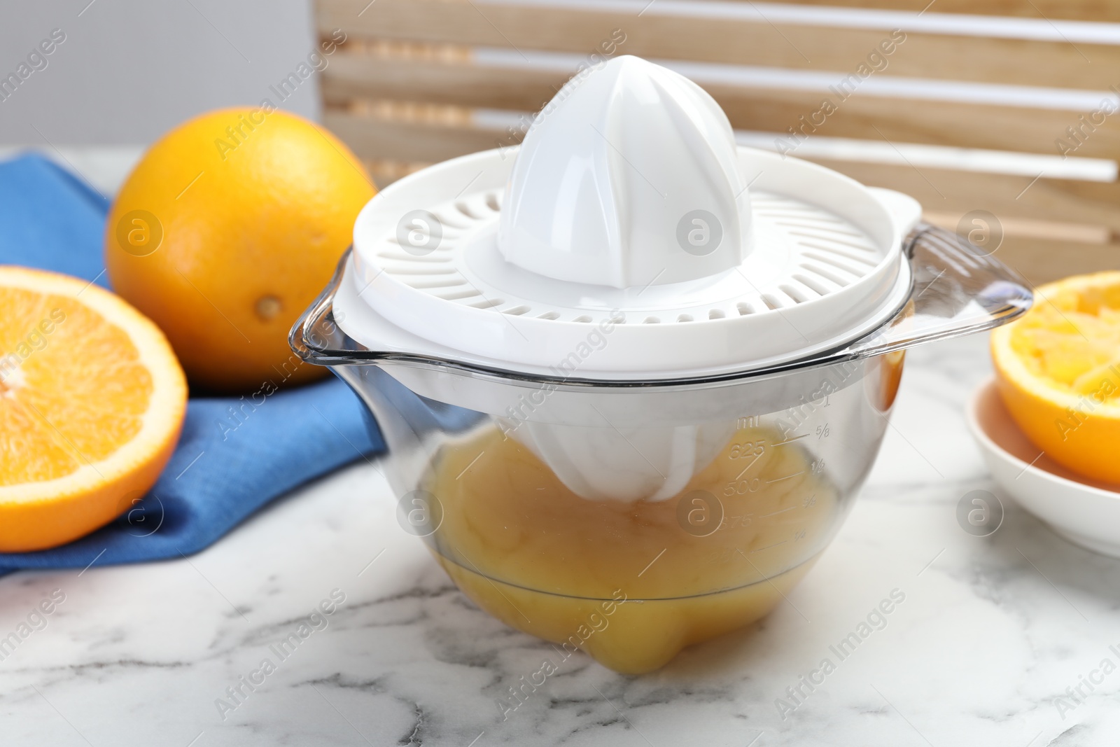 Photo of Plastic juicer and fresh oranges on white marble table, closeup