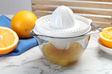 Photo of Plastic juicer and fresh oranges on white marble table, closeup