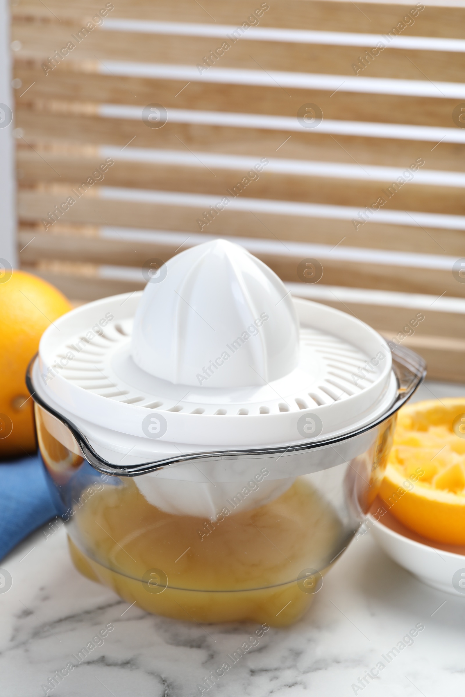 Photo of Plastic juicer and fresh oranges on white marble table, closeup