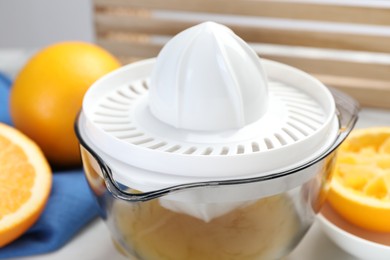 Photo of Plastic juicer and fresh oranges on white table, closeup