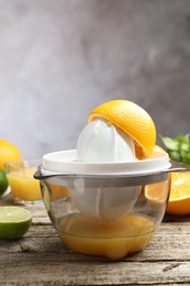 Photo of Plastic juicer and fresh oranges on wooden table, closeup